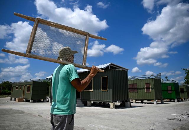 A worker carries a wooden frame across a construction site with housing units made from shipping containers in Havana on May 7, 2026. Amid a housing deficit exceeding 800,000 homes, Cuba has begun converting shipping containers into housing units. Initially intended to transport equipment for solar parks, these metal modules are now being adapted as homes for vulnerable groups, including families affected by climate events, recipients of state subsidies and young people without family support. (Photo by YAMIL LAGE / AFP)