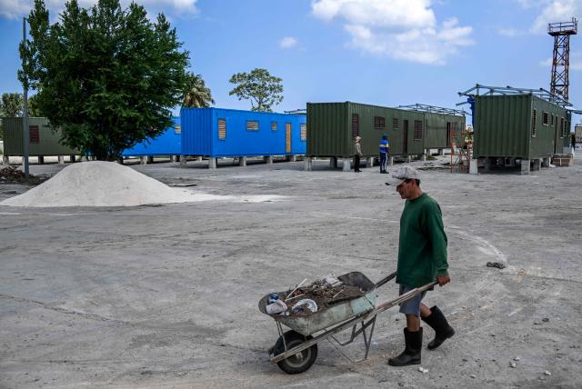 A worker pushes a wheelbarrow across a construction site with housing units made from shipping containers in Havana on May 7, 2026. Amid a housing deficit exceeding 800,000 homes, Cuba has begun converting shipping containers into housing units. Initially intended to transport equipment for solar parks, these metal modules are now being adapted as homes for vulnerable groups, including families affected by climate events, recipients of state subsidies and young people without family support. (Photo by YAMIL LAGE / AFP)
