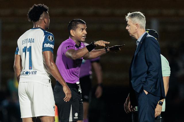 Venezuelan referee Alexis Herrera speaks with Liga de Quito's Brazilian head coach Tiago Nunes and Mirassol's head coach Rafael Guanaes (behind) during the Copa Libertadores group stage football match between Brazil's Mirassol and Ecuador's Liga de Quito at the Jose Maria de Campos Maia stadium in Mirassol, state of Sao Paulo, Brazil on May 7, 2026. (Photo by RAPHA MARQUES / AFP)