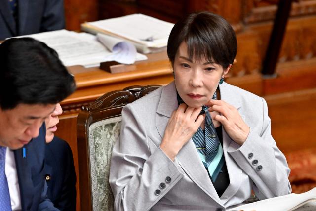 Japan's Prime Minister Sanae Takaichi (R) removes a scarf as she was wearing around her neck during a plenary session of the House of Councillors to deliberate on the bill to establish the National Intelligence Council at parliament in Tokyo on May 8, 2026. (Photo by Kazuhiro NOGI / AFP)