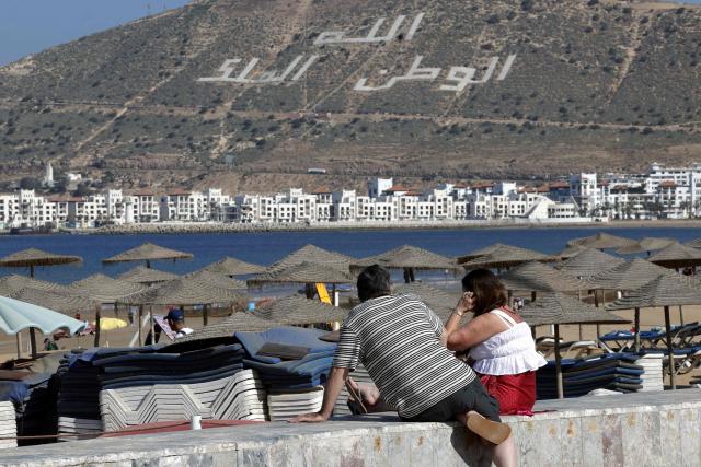 The words ‘Allah, Country and the King’ is seen on the hillside overlooking the Agadir Corniche that runs along the Atlantic Ocean, as people sit looking out at sea along the promenade in the city of Agadir on May 7, 2026. This promenade is very popular with locals, visitors, and tourists, especially for walking, sports, and leisure activities. (Photo by Abdel Majid BZIOUAT / AFP)