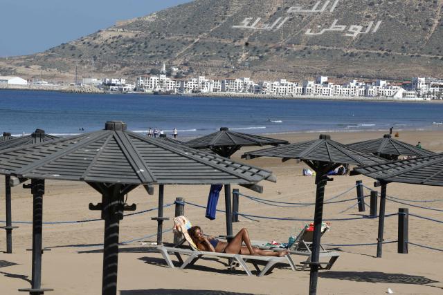 The words ‘Allah, Country and the King’ is seen on the hillside overlooking the Agadir Corniche that runs along the Atlantic Ocean, as a woman sunbathes on a beach in the city of Agadir on May 7, 2026. This promenade is very popular with locals, visitors, and tourists, especially for walking, sports, and leisure activities. (Photo by Abdel Majid BZIOUAT / AFP)