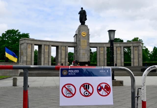 A sign by the police in Berlin indicating the prohibition of uniforms, insignia of rank and the display of Russian and Soviet flags are fixed at a fence as a Ukrainian flag flies at the Soviet War Memorial Tiergarten in Berlin on May 8, 2026 ahead a ceremony in commemoration of the anniversary of the 1945 victory against Nazi Germany. (Photo by John MACDOUGALL / AFP)