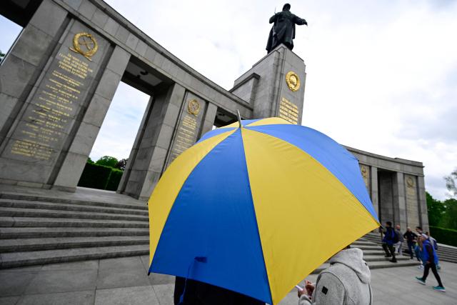 A man holding an umbrella with colours of the Ukrainian flag stands at the Soviet War Memorial Tiergarten in Berlin on May 8, 2026 ahead a ceremony in commemoration of the anniversary of the 1945 victory against Nazi Germany. (Photo by John MACDOUGALL / AFP)