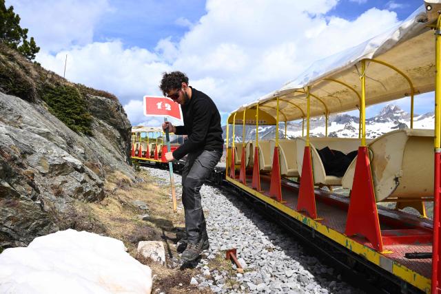 An employee installs a sign next to the railway line to allow the little train, a historic tourist railway, to pass in Artouste near Laruns, south-western France, on May 7, 2026. The Artouste little train is located in the Ossau Valley, in the Pyrenees-Atlantiques department of France. This historic tourist railway offers a mountain excursion at an altitude of over 2,000 meters. It travels 10 kilometers on its narrow-gauge track. It is the highest narrow-gauge railway in Europe. (Photo by Gaizka IROZ / AFP)