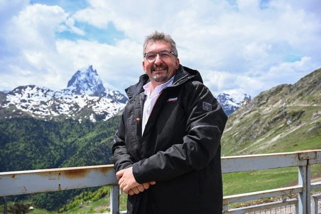 Director of the Artouste ski resort and train Jean-Christophe Lalanne poses with the Pic d'Ossau mountain peak of the Pyrenees in Artouste near Laruns, south-western France, on May 7, 2026. The Artouste little train is located in the Ossau Valley, in the Pyrenees-Atlantiques department of France. This historic tourist railway offers a mountain excursion at an altitude of over 2,000 meters. It travels 10 kilometers on its narrow-gauge track. It is the highest narrow-gauge railway in Europe. (Photo by Gaizka IROZ / AFP)