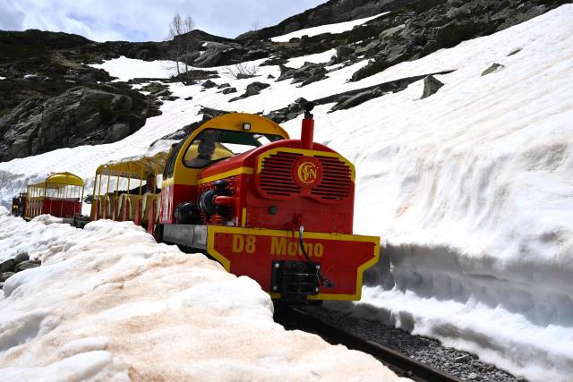 This photograph shows a view of the little train of Artouste, a historic tourist railway,  passing between snow on the mountainside ahead of its opening to the public on May 8th in Artouste near Laruns, south-western France, on May 7, 2026. The Artouste little train is located in the Ossau Valley, in the Pyrenees-Atlantiques department of France. This historic tourist railway offers a mountain excursion at an altitude of over 2,000 meters. It travels 10 kilometers on its narrow-gauge track. It is the highest narrow-gauge railway in Europe. (Photo by Gaizka IROZ / AFP)