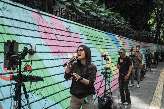 Online buskers use a colourful wall as a backdrop as they perform on a sidewalk to attract viewers for digital donations during their livestreams on social media sites in Bandung, West Java, on May 8, 2026. The singers performing on social media video streaming sites earn on average 4-10 USD from digital payments over three hours of performing. (Photo by TImur Matahari / AFP)