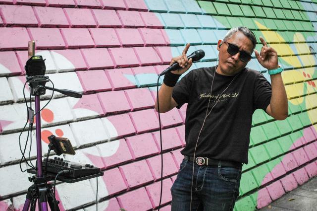 An online busker uses a colourful wall as a backdrop as they perform on a sidewalk to attract viewers for digital donations during their livestreams on social media sites in Bandung, West Java, on May 8, 2026. The singers performing on social media video streaming sites earn on average 4-10 USD from digital payments over three hours of performing. (Photo by TImur Matahari / AFP)
