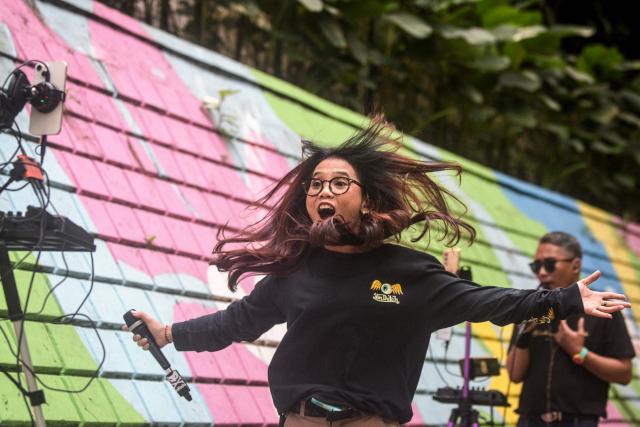 Online buskers use a colourful wall as a backdrop as they perform on a sidewalk to attract viewers for digital donations during their livestreams on social media sites in Bandung, West Java, on May 8, 2026. The singers performing on social media video streaming sites earn on average 4-10 USD from digital payments over three hours of performing. (Photo by TImur Matahari / AFP)