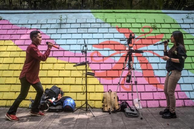 Online buskers use a colourful wall as a backdrop as they perform on a sidewalk to attract viewers for digital donations during their livestreams on social media sites in Bandung, West Java, on May 8, 2026. The singers performing on social media video streaming sites earn on average 4-10 USD from digital payments over three hours of performing. (Photo by TImur Matahari / AFP)