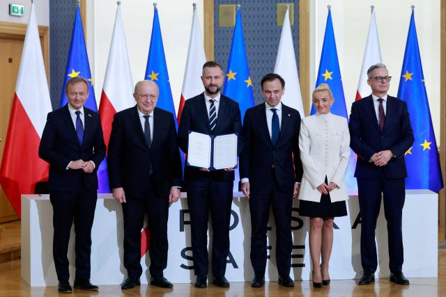 Polish Deputy Prime Minister and Defence Minister Wladyslaw Kosiniak Kamysz (3rdL) poses with the document of the signed SAFE loan agreement between the European Union and Poland next to Polish Finance Minister Andrzej Domanski (3rdR) and EU Commissioner Andrius Kubilius (2ndL), First Vice President of the Management Board of Polish development bank BGK Marta Postula (2ndR), President of the Management Board of BGK Miroslaw Czekaj (R) and EU Commissioner for Budget, Anti-Fraud and Public Administration Piotr Serafin (L) at the Chancellery of the Polish Prime Minister in Warsaw on May 8, 2026. Poland participates in the new EU programme called SAFE (Security Action For Europe) that came into effect last year and under which countries can get EU loans to buy weapons and expand defence manufacturing. (Photo by Wojtek RADWANSKI / AFP)