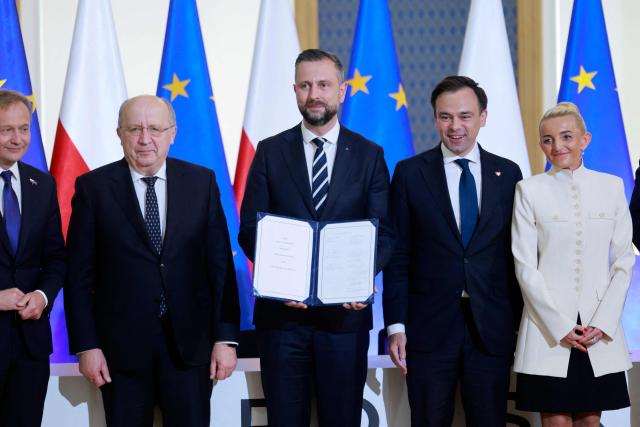 Polish Deputy Prime Minister and Defence Minister Wladyslaw Kosiniak Kamysz (C) poses with the document of the signed SAFE loan agreement between the European Union and Poland next to Polish Finance Minister Andrzej Domanski (2ndR) and EU Commissioner Andrius Kubilius (2ndL), First Vice President of the Management Board of Polish development bank BGK Marta Postula (R) and EU Commissioner for Budget, Anti-Fraud and Public Administration Piotr Serafin at the Chancellery of the Polish Prime Minister in Warsaw on May 8, 2026. Poland participates in the new EU programme called SAFE (Security Action For Europe) that came into effect last year and under which countries can get EU loans to buy weapons and expand defence manufacturing. (Photo by Wojtek RADWANSKI / AFP)