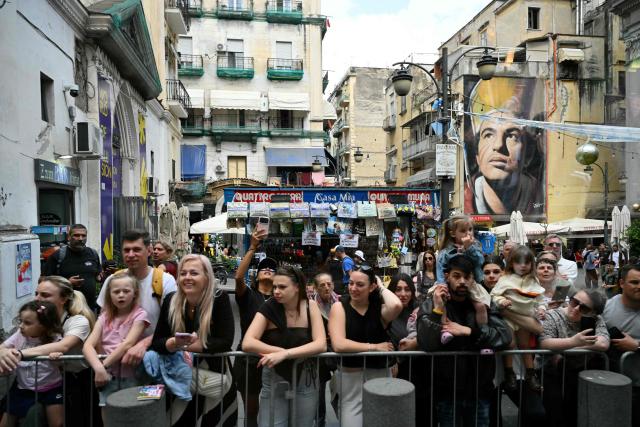 People stand behind barriers in the "Spaccanapoli" area, with the San Gennaro mural by Jorit Agoch in the background, as they wait to see Pope Leo XIV as part of a pastoral visit in Naples on 8 May 2026.  (Photo by Alberto PIZZOLI / AFP)