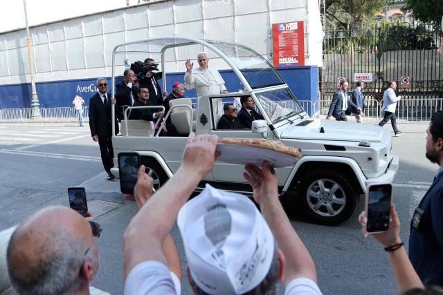 A man holds a pizza as Pope Leo XIV waves to people on his way to the Piazza del Plebiscito for a holy mass as part of a pastoral visit in Naples on May 8, 2026. (Photo by Carlo Hermann / AFP)