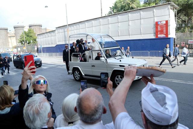 A man holds a pizza as Pope Leo XIV waves to people on his way to the Piazza del Plebiscito for a holy mass as part of a pastoral visit in Naples on May 8, 2026. (Photo by Carlo Hermann / AFP)