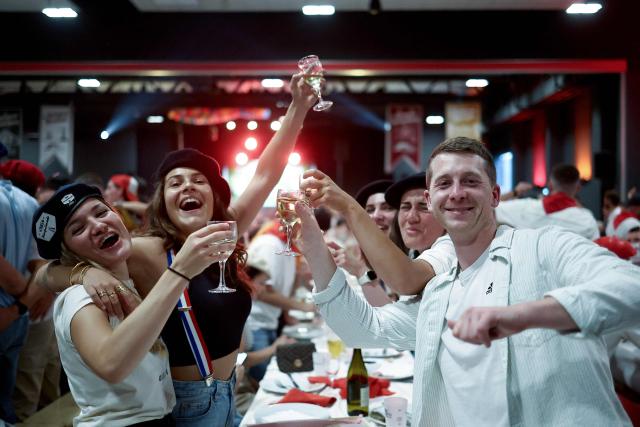People toast with drinks during a big banquet organised by the 'Canon francais' in Montelimar, south-eastern France, on May 8, 2026. The banquets of the 'Canon francais', which draw thousands of guests around roast pork and red wine to "promote local traditions and heritage," are accused by their critics of spreading racist ideas behind their patriotic, typically French image. (Photo by Alex MARTIN / AFP)