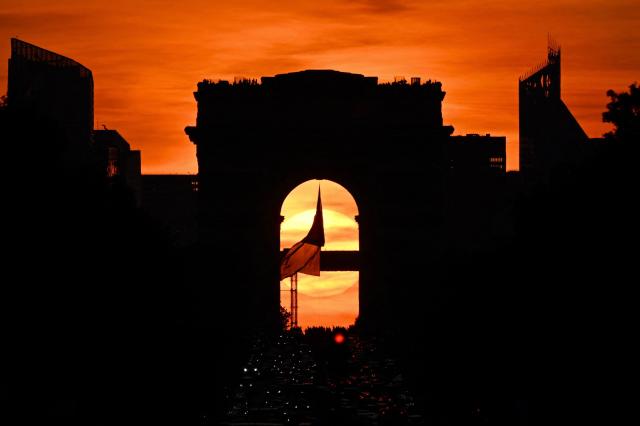 This photograph shows the French national flag waving under the Arc de Triomphe monument on the Avenue des Champs Elysees during the "Paris henge" phenomenon in Paris, on May 8, 2026. This phenomenon happens twice a year at sunset when the sun aligns between the Arc de Triomphe monument and the last rays of sunlight on the Champs Elysees in Paris. (Photo by Christophe DELATTRE / AFP)