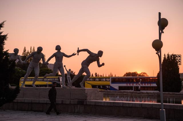 A pedestrian walks past statues of athletes on a street outside the Pyongyang Ice Rink in Pyongyang on May 8, 2026. (Photo by KIM Won Jin / AFP)