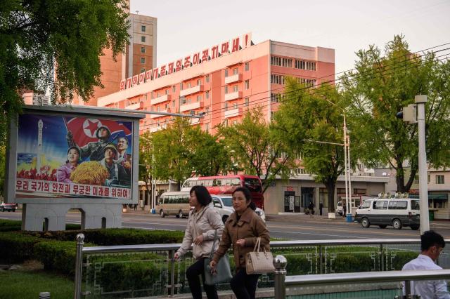 Pedestrians walk past a mural (L) that reads "For the safety and endless future of our nation", as a building adorned with the slogan "Long live the great people-first politics" is seen in the background in Pyongyang on May 8, 2026. (Photo by KIM Won Jin / AFP)