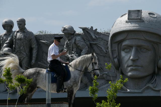A Russian police officer uses his mobile phone as he rides a horse past a monument during a ceremony marking the 81st anniversary of the victory over Nazi Germany in World War II at the Savur-Mohyla memorial in the Donetsk region, Russian-controlled Ukraine on May 8, 2026, amid the ongoing Russian-Ukrainian conflict. (Photo by AFP)