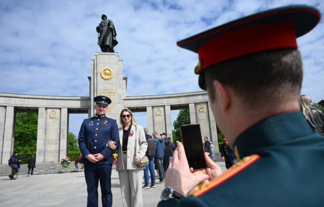 A man in a soldier's uniform and a woman pose for photos as they pay their respect at the Soviet War Memorial Tiergarten in Berlin on May 9, 2026, the 81st anniversary of the 1945 victory against Nazi Germany. (Photo by RALF HIRSCHBERGER / AFP)