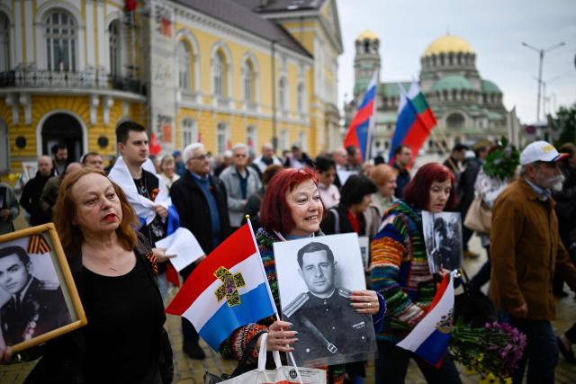 People hold portraits and wave Russian and Bulgarian flags during an "Immortal Regiment" march celebrating the Victory Day, marking the Allied victory against Nazi Germany and the end of World War II in Europe (VE Day), in Sofia, on May 9, 2026. Pro-Russian circles in Bulgaria remain divided over the prospects for improved relations with Russia following Rumen Radev’s assumption of the office of prime minister. (Photo by Nikolay DOYCHINOV / AFP)