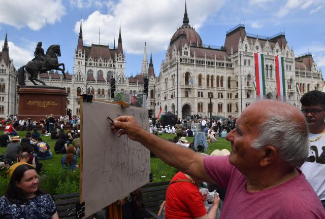 A man draws a picture as people gather in front of Hungary's parliament building in Budapest on May 9, 2026. Pro-European conservative Peter Magyar will be officially sworn in as Prime Minister by the Hungarian parliament on May 9, 2026, just under a month after his landslide victory in the parliamentary elections against nationalist Viktor Orban. (Photo by Ferenc ISZA / AFP)