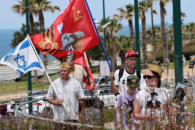Red Army veterans participate alongside relatives and supporters carry flags during a ceremony to commemorate the 81th anniversary of the Victory over Germany in World War II, at the Victory Monument commemorating the Red Army's victory over Nazi Germany, in the Israeli coastal city of Netanya on May 9, 2026. (Photo by JACK GUEZ / AFP)