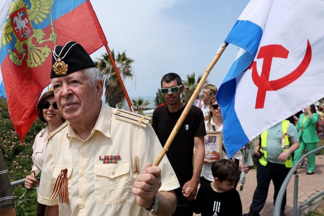 Red Army veterans participate alongside relatives and supporters wave flags and hold up portraits during a ceremony to commemorate the 81th anniversary of the Victory over Germany in World War II, at the Victory Monument commemorating the Red Army's victory over Nazi Germany, in the Israeli coastal city of Netanya on May 9, 2026. (Photo by JACK GUEZ / AFP)