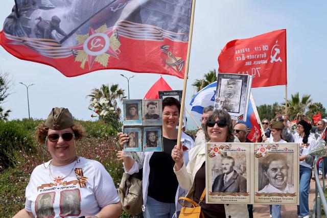 Red Army veterans participate alongside relatives and supporters wave flags and hold up portraits during a ceremony to commemorate the 81th anniversary of the Victory over Germany in World War II, at the Victory Monument commemorating the Red Army's victory over Nazi Germany, in the Israeli coastal city of Netanya on May 9, 2026. (Photo by JACK GUEZ / AFP)