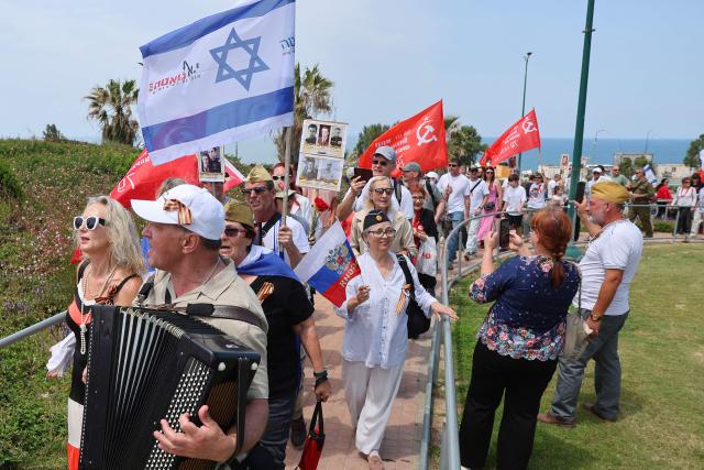 Red Army veterans participate alongside relatives and supporters wave flags and hold up portraits during a ceremony to commemorate the 81th anniversary of the Victory over Germany in World War II, at the Victory Monument commemorating the Red Army's victory over Nazi Germany, in the Israeli coastal city of Netanya on May 9, 2026. (Photo by JACK GUEZ / AFP)