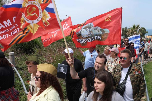 Red Army veterans participate alongside relatives and supporters wave flags and hold up portraits during a ceremony to commemorate the 81th anniversary of the Victory over Germany in World War II, at the Victory Monument commemorating the Red Army's victory over Nazi Germany, in the Israeli coastal city of Netanya on May 9, 2026. (Photo by JACK GUEZ / AFP)