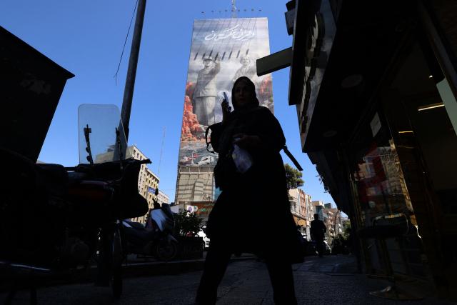 A woman walks along a busy street near a huge mural painted on the side of a building referring to the 'Strait of Hormuz', in the capital Tehran on May 9, 2026. Iran questioned the seriousness of American diplomacy on May 9, in the wake of renewed naval clashes in the Gulf, while keeping Washington waiting for a response to its latest negotiating position. On February 28, 2026, Israel and the United States launched strikes on Iran, killing its supreme leader and triggering a war that spread across the Middle East. (Photo by ATTA KENARE / AFP) / 