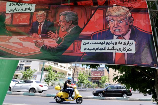 An Iranian man rides his moped past a banner depicting a cartoon of the US president which reads, 'So we go for the freedom of Iranian women' (L) and 'There is no need for a video, I will do what ever you say' (R),  in the capital Tehran on May 9, 2026. Iran questioned the seriousness of American diplomacy on May 9, in the wake of renewed naval clashes in the Gulf, while keeping Washington waiting for a response to its latest negotiating position. On February 28, 2026, Israel and the United States launched strikes on Iran, killing its supreme leader and triggering a war that spread across the Middle East. (Photo by ATTA KENARE / AFP) / 