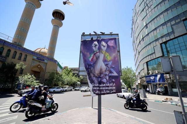 Motorbikes drives past a banner depicting an Iranian fist (L) and a Lebanese Shia Muslim party Hezbollah fist punching through an Israeli  Star of David, hangs on a street in the capital Tehran on May 9, 2026. Iran questioned the seriousness of American diplomacy on May 9, in the wake of renewed naval clashes in the Gulf, while keeping Washington waiting for a response to its latest negotiating position. On February 28, 2026, Israel and the United States launched strikes on Iran, killing its supreme leader and triggering a war that spread across the Middle East. (Photo by ATTA KENARE / AFP) / 
