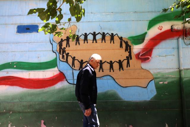 An Iranian man walks past the map of Iran, with its citizens holding hands, painted on a wall in the capital Tehran on May 9, 2026. Iran questioned the seriousness of American diplomacy on May 9, in the wake of renewed naval clashes in the Gulf, while keeping Washington waiting for a response to its latest negotiating position. On February 28, 2026, Israel and the United States launched strikes on Iran, killing its supreme leader and triggering a war that spread across the Middle East. (Photo by ATTA KENARE / AFP) / 