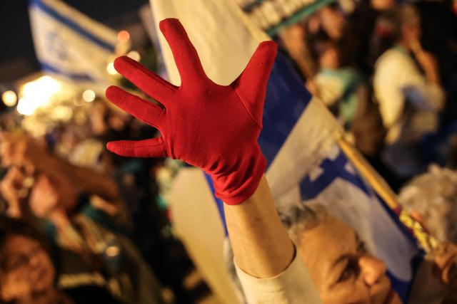 An Israeli left-wing activist raises a red-gloved hand during a rally in Tel Aviv's HaBima Square against the ongoing war with Iran and against the Israeli government on May 9, 2026. The war, launched by the United States and Israel in late February, has seen Iran respond with attacks across the Middle East and impose a chokehold on the Strait of Hormuz, the gateway to the Gulf oil and gas industries and a strategic trade route. (Photo by Jack GUEZ / AFP) / 