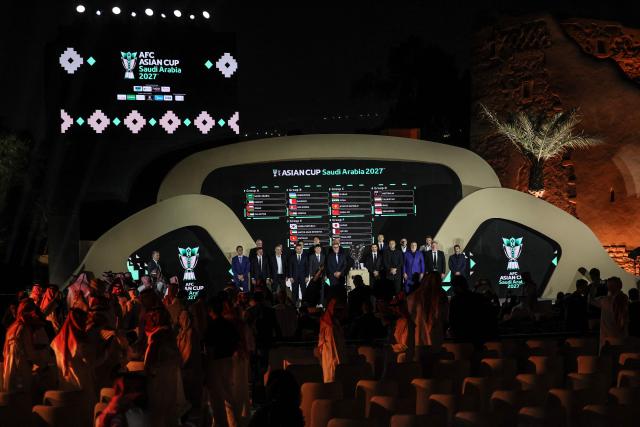 Coaches of Asian national football teams pose in front of a screen showing the results of the final draw for the 2027 AFC Asian Cup during a ceremony in Diriyah, on the outskirts of Riyadh, on May 9, 2026. The 19th edition of the Asian Cup is scheduled to take place from January 7 to February 5 next year in Saudi Arabia. (Photo by Fayez NURELDINE / AFP)