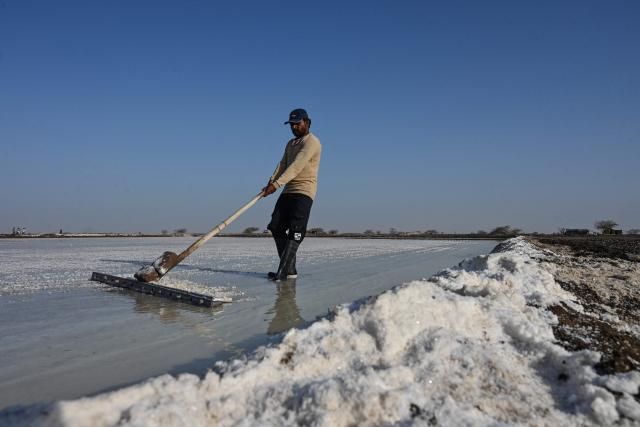 This photograph taken on April 29, 2026 shows a salt pan worker raking harvested salt at an alkali flat in the Little Rann of Kutch region in Gujarat. India faces challenging heatwaves each year, but few places endure conditions as searing as the country's western desert salt pans, where workers rely on simple techniques to survive almost unbearable temperatures. In Gujarat's Little Rann of Kutch summer temperatures routinely cross 45 degrees Celsius (113 Fahrenheit), and can climb to 4748C. Up to 50,000 workers spend eight months on the remote salt pans without electricity or healthcare, relying on a tanker to deliver drinking and washing water every 25 days. (Photo by Shammi MEHRA / AFP) / TO GO WITH 'India-Climate-Health' FOCUS