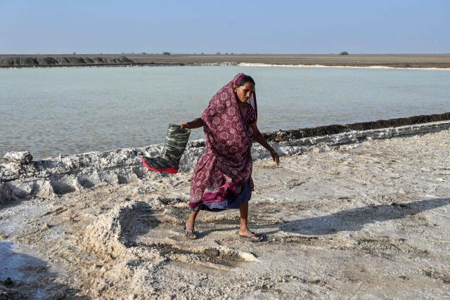 This photograph taken on April 29, 2026 shows a salt pan worker carrying rubber boots as she walks across an alkali flat at the Little Rann of Kutch region in Gujarat. India faces challenging heatwaves each year, but few places endure conditions as searing as the country's western desert salt pans, where workers rely on simple techniques to survive almost unbearable temperatures. In Gujarat's Little Rann of Kutch summer temperatures routinely cross 45 degrees Celsius (113 Fahrenheit), and can climb to 4748C. Up to 50,000 workers spend eight months on the remote salt pans without electricity or healthcare, relying on a tanker to deliver drinking and washing water every 25 days. (Photo by Shammi MEHRA / AFP) / TO GO WITH 'India-Climate-Health' FOCUS