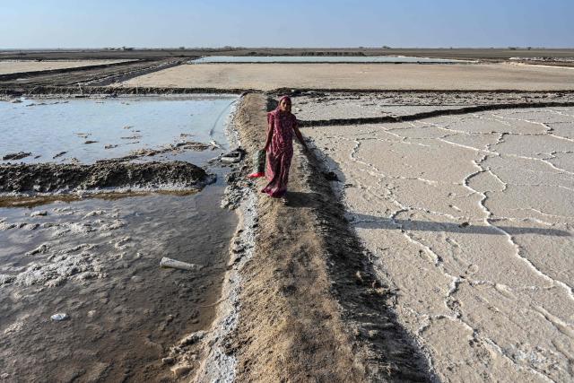 This photograph taken on April 29, 2026 shows a salt pan worker carrying rubber boots as she walks across an alkali flat at the Little Rann of Kutch region in Gujarat. India faces challenging heatwaves each year, but few places endure conditions as searing as the country's western desert salt pans, where workers rely on simple techniques to survive almost unbearable temperatures. In Gujarat's Little Rann of Kutch summer temperatures routinely cross 45 degrees Celsius (113 Fahrenheit), and can climb to 4748C. Up to 50,000 workers spend eight months on the remote salt pans without electricity or healthcare, relying on a tanker to deliver drinking and washing water every 25 days. (Photo by Shammi MEHRA / AFP) / TO GO WITH 'India-Climate-Health' FOCUS