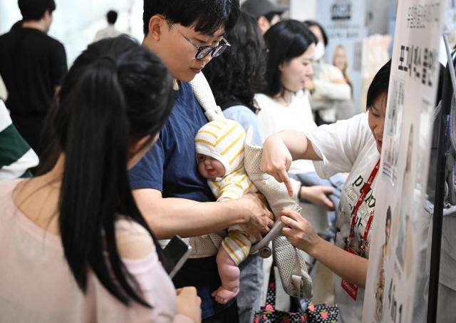This picture taken on April 30, 2026 shows a man testing a baby carrier using a baby doll at a booth during a baby fair in Seoul. South Korea has one of the world's lowest birth rates, and the government has spent billions of dollars trying to encourage citizens to have more babies and cushion the worst impacts of a shrinking population. The Asian nation is still nowhere near reversing the trend, but a modest baby bump is offering a glimmer of hope after years of bleak statistics. (Photo by Jung Yeon-je / AFP) / TO GO WITH AFP STORY  SKorea-demographics / FOCUS BY Matthew Walsh and Jihye Shin