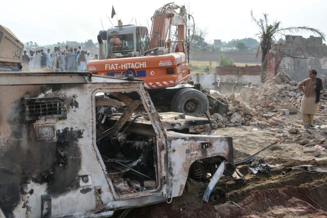 People gather around a burned armored vehicle at the damaged police checkpost following a car bombing attack by militants in the Fateh Khel area of Pakistan's Bannu on May 10, 2026. Militants detonated a car bomb at a checkpoint in northwestern Pakistan and opened fire on police, killing at least 12 and wounding five, officials said on May 10. (Photo by Karim ULLAH / AFP)