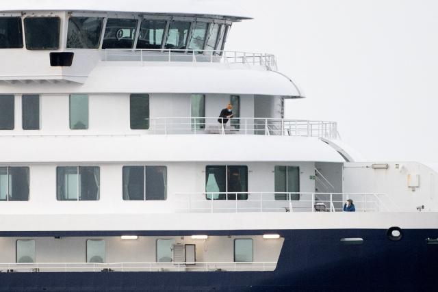 A passenger stands on a balcony of the Dutch flagged hantavirus-stricken cruise ship MV Hondius as it arrives to the industrial port of Granadilla de Abona on the island of Tenerife in Spain's Canary Islands to commence evacuation of passengers and most crew members on May 10, 2026. Repatriation flights for the nearly 150 passengers onboard the ship hit by a deadly hantavirus outbreak are planned to the United States, Britain, France,  and other countries, Spain's interior minister announced on Saturday. Spanish authorities have said the ship will anchor off Tenerife and will not be allowed to dock. Most of the nearly 150 people on board will be transferred to shore on smaller vessels then by bus to the airport and then flown home after weeks at sea. (Photo by JORGE GUERRERO / AFP)