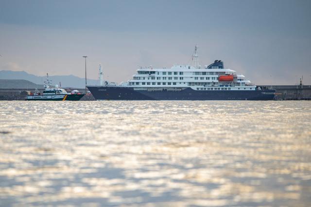 The Dutch flagged hantavirus-stricken cruise ship MV Hondius arrives to the industrial port of Granadilla de Abona on the island of Tenerife in Spain's Canary Islands to commence evacuation of passengers and most crew members on May 10, 2026. Repatriation flights for the nearly 150 passengers onboard the ship hit by a deadly hantavirus outbreak are planned to the United States, Britain, France,  and other countries, Spain's interior minister announced on Saturday. Spanish authorities have said the ship will anchor off Tenerife and will not be allowed to dock. Passengers will be transferred to shore on a smaller vessel then by bus to the airport and then flown home after weeks at sea. (Photo by Antonio Sempere / AFP)