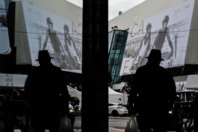 A pedestrian is reflected as he walks in front of the official poster of the 78th Cannes Film Festival on the facade of the Palais des Festivals in Cannes, south-eastern France on May 10, 2026. The Cannes Film festival is scheduled to take place from May 12 to May 23. (Photo by Valery HACHE / AFP)