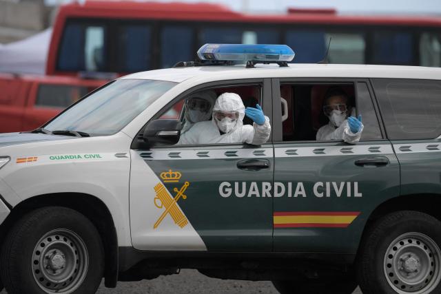 Spanish civil guards wearing hazmat protective suits signal from their car during the operation to transfer passengers from the Dutch flagged hantavirus-stricken cruise ship MV Hondius at the industrial port of Granadilla de Abona on the island of Tenerife in Spain's Canary Islands on May 10, 2026. Repatriation flights for the nearly 150 passengers onboard the ship hit by a deadly hantavirus outbreak began as passengers were transferred to shore on smaller vessels then by bus to the airport to be flown home after weeks at sea. (Photo by JORGE GUERRERO / AFP)