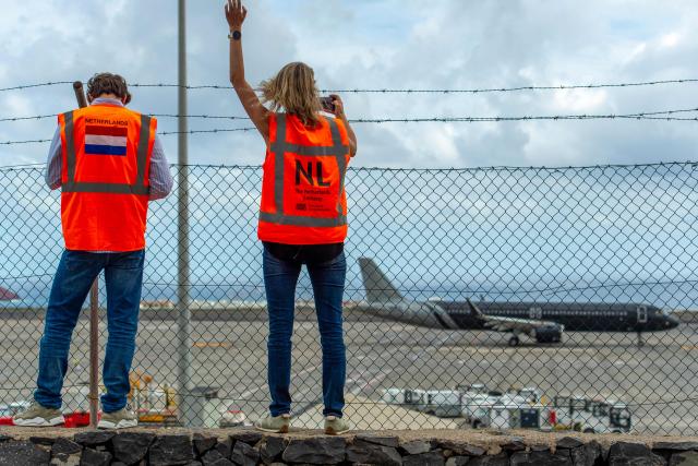 Representatives from the Netherlands embassy wave as a plane bound for the Netherlands carrying passengers evacuated from the Dutch flagged hantavirus-stricken cruise ship MV Hondius prepares to take off from the Tenerife Sur-Reina Sofia airport on the island of Tenerife in Spain's Canary Islands on May 10, 2026. Repatriation flights for the nearly 150 passengers onboard the ship hit by a deadly hantavirus outbreak got underway as passengers and some crew members were transferred to shore on smaller vessels then by bus to the airport and then flown home after weeks at sea. (Photo by Antonio Sempere / AFP)