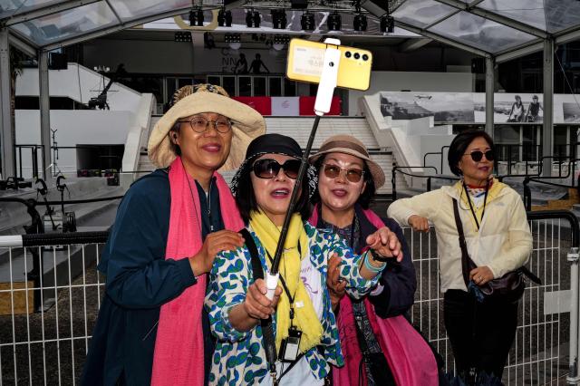 Pedestrians take a selfie in front of the official poster of the 79th edition of the Cannes Film Festival displayed on the facade of the Palais des Festivals in Cannes, south-eastern France on May 10, 2026. The Cannes Film festival will take place from May 12, 2026 to May 23, 2026. (Photo by Valery HACHE / AFP)